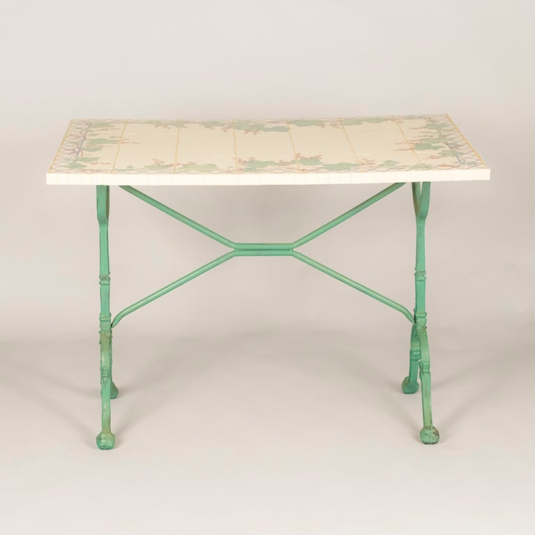 A French Bistro Table with a light green painted base and a hand painted tile top with red currant and leaf motifs. The tiling and painted top is signed by the artist Brigitte Gangloff.