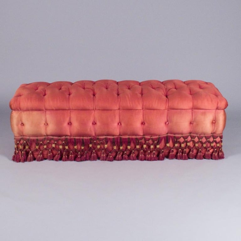 A French Boudoir Banquette in hot pink padded and tufted upholstery. The fringe has burgundy, dark brown and beige tones. The feet are beech wood.