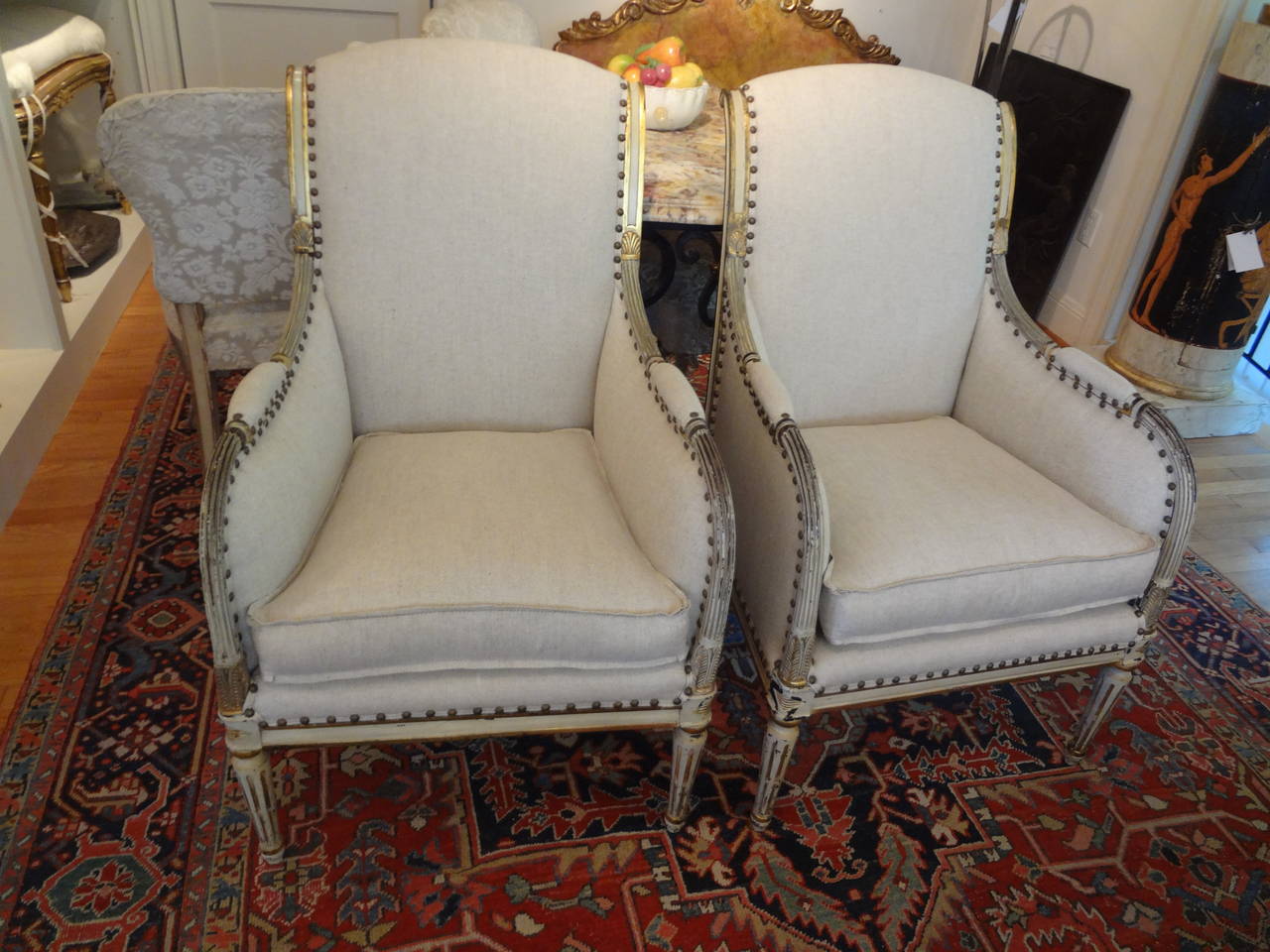 Gorgeous pair of Swedish Gustavian Style painted and gilt bergeres. Professionally upholstered in oatmeal linen with down wrapped cushion and spaced French brass nailhead detail.

Please click KIRBY ANTIQUES logo below to view additional pieces