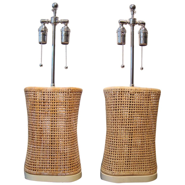 Pair of 1950's woven rattan table lamps; shape and design are inspired by a Japanese pillow.  Lamps retain original ivory lacquered bases and caps, and have been outfitted with new nickel hardware.  A light, airy, organic design.