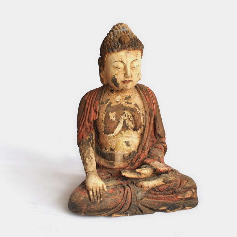 A well carved, polychrome wood figure of a seated cross legged Buddha, wearing draped monk's robes. The face is finely carved with gentle meditating expression and hair consisting of spiraling curls. Its provenance is from the ancient town of Huang