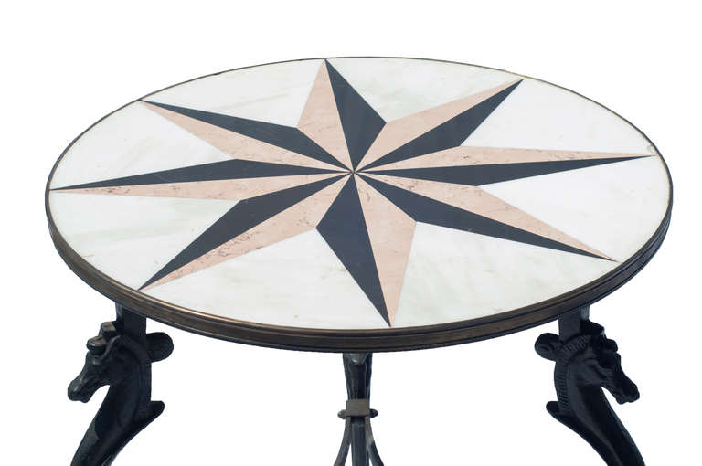A cast iron gueridon table with an inlay marble top and horse head decoration on the cast iron base.