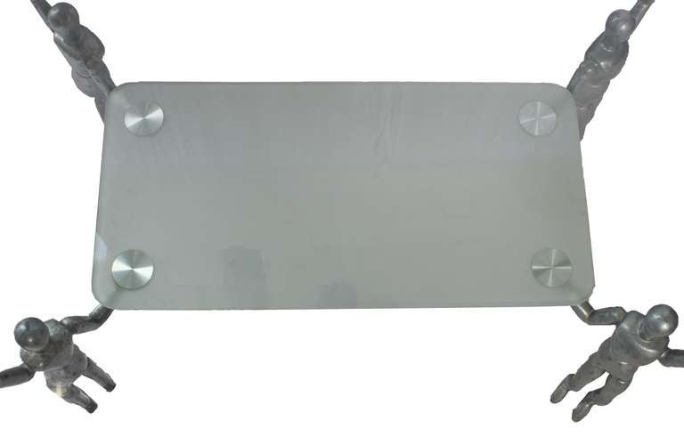 A Modern Glass Top Coffee Table with a  Lower Frosted Glass Shelf with Four Metal Alloy Mannequin Supports.