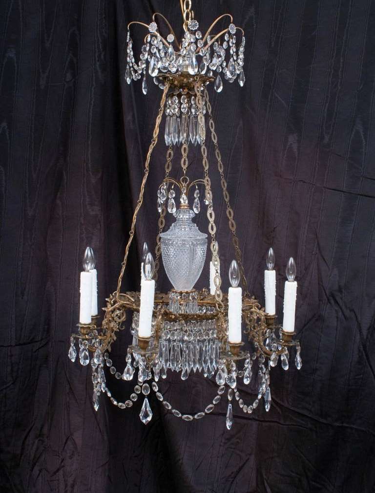 The hand-cast and gilt metal frame is a foliate design with acorns and oak leaves on each arm. A hand-cut crystal urn-shaped pendant hangs free in the center of the fixture. Most of the crystal prisms on this chandelier are original and are in their