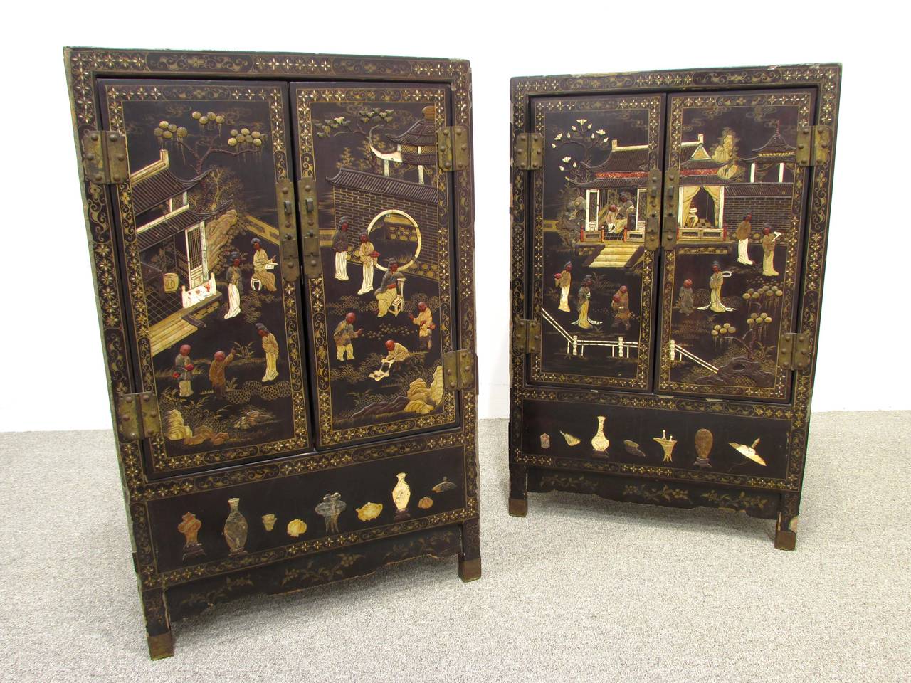 Distressed pair of black lacquered cabinets with inlaid hardstone and bone figures in palace setting with red lacquered interiors with brass accents and locks