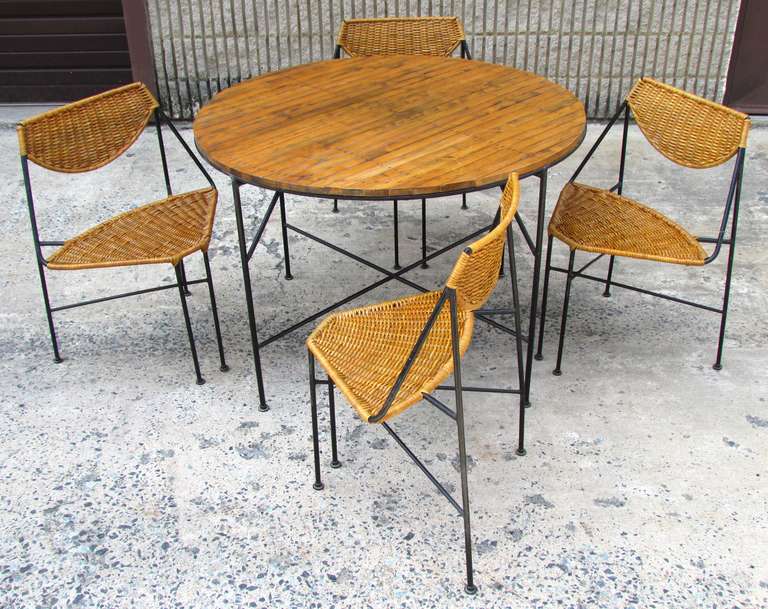 Beautiful dining set with wooden slat table over iron base and four wicker wrapped iron wedge shaped chairs by Arthur Umanoff

Table 29.5