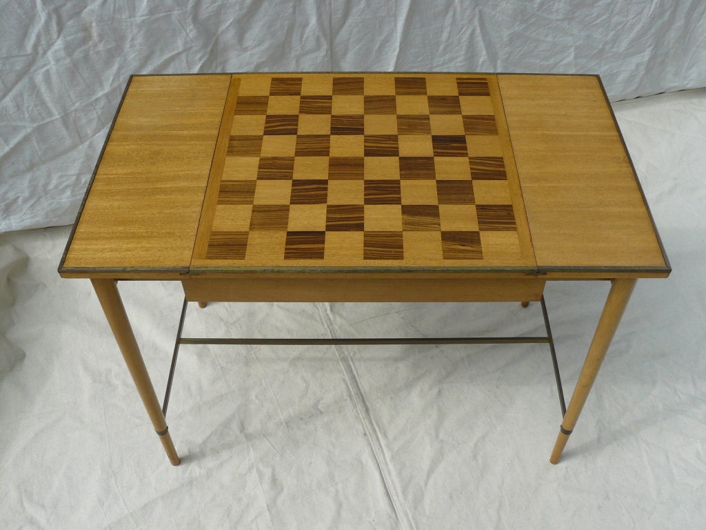 50's Paul McCobb for H Sacks & Sons reversible top game table. Bleached mahogany raised on tapered legs with brass stretchers, the top center section has a chess/checker game table pattern in mahogany and macassar ebony inlay which slides out and