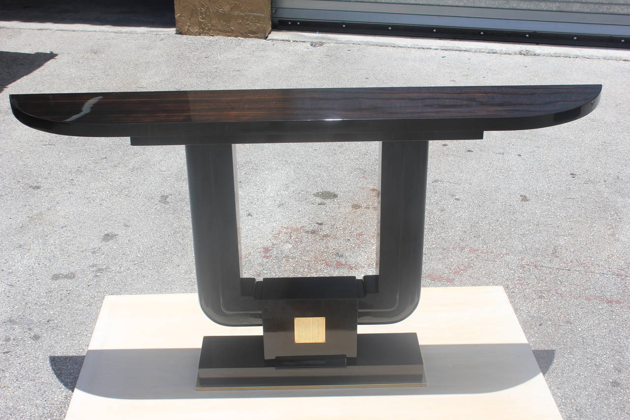 A spectacular French Art Deco Exotic Macassar Ebony with ebony Demilune Console Table, circa 1940's. Demi lune top on steeped macassar support, center macassar square base with brass plaque. Ebony finish on u shaped support. Brass encased base.