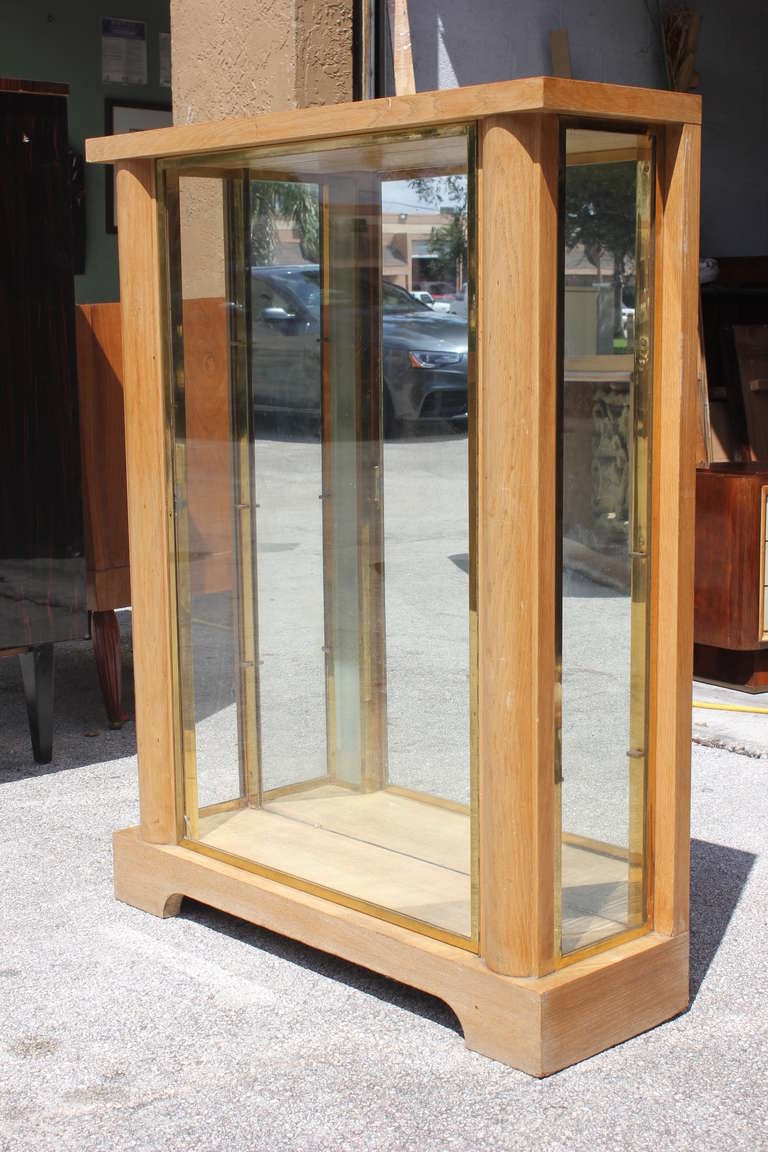 A French Art Deco Designer Ceruse Oak Curio Cabinet. Brass encased glass with interior glass shelves. By Kohlman Etienne.