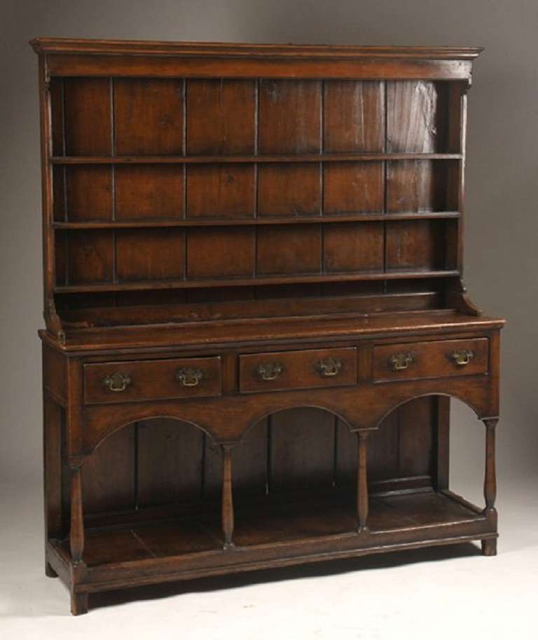 Late eighteenth century English oak Welsh cupboard having stepped back plate rack top over lower server with three drawers. Supported on turned legs and lower shelf. Ht: 73.5