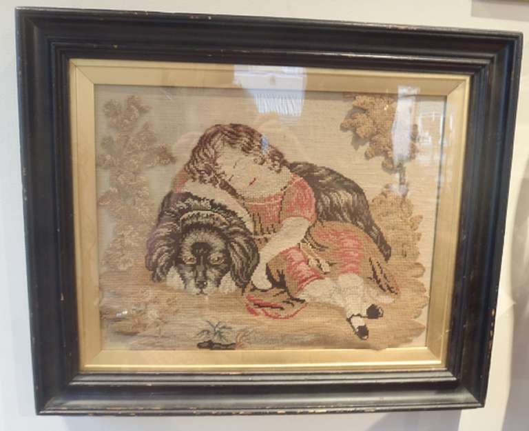A framed Victorian needlepoint work picturing a young girl asleep upon her dog.
