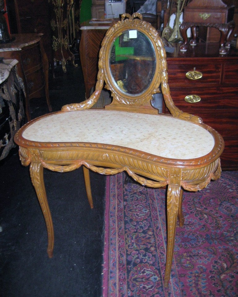 Louis XV style carved walnut vanity, having an oval beveled glass mirror in a leaf and ribbon carved frame surmounting a kidney-shape table on leaf carved tapering legs.