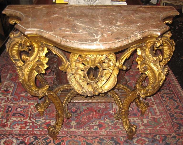A very fine Louis XV carved gilt-wood marble top console table, having a shaped Basque Jaspe molded marble top over a conforming frieze above four carved scroll and foliate legs with 'X' form stretch support on scroll toe feet.