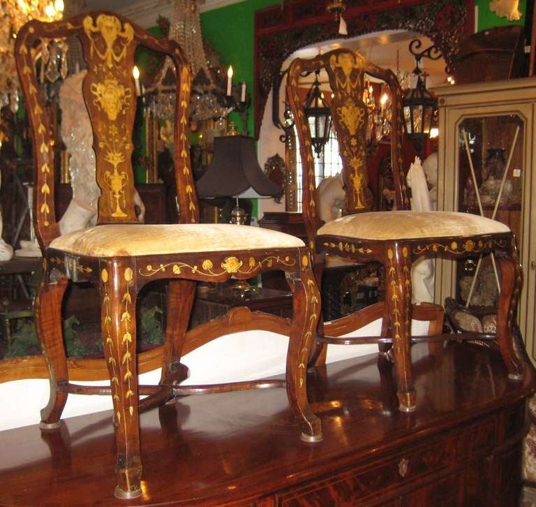 Pair of Dutch marquetry inlaid side chairs, having a shaped splat back inlaid with a mask above a crowned shield over a flowering urn and foliate trails throughout raised on tapering carbriole legs joined by a shaped x-form stretcher. This is a