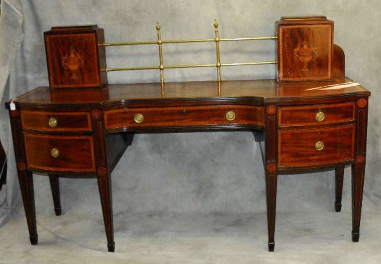 Rare Georgian mahogany and satinwood inlaid sideboard, the shaped rectangular banded inlaid top surmounted with a brass gallery rail flanked by a pair of urn inlaid revolving knife boxes above a banded inlaid center drawer and flanked by four