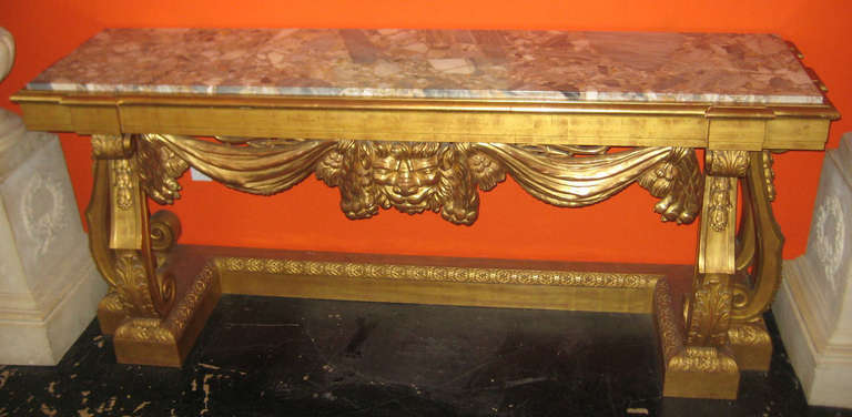 Continental carved gilt-wood marble top console table, having a long rectangular inset marble top above a plain and lion form drapery frieze on square scroll molded legs with carved acanthus leaves on a plinth base.