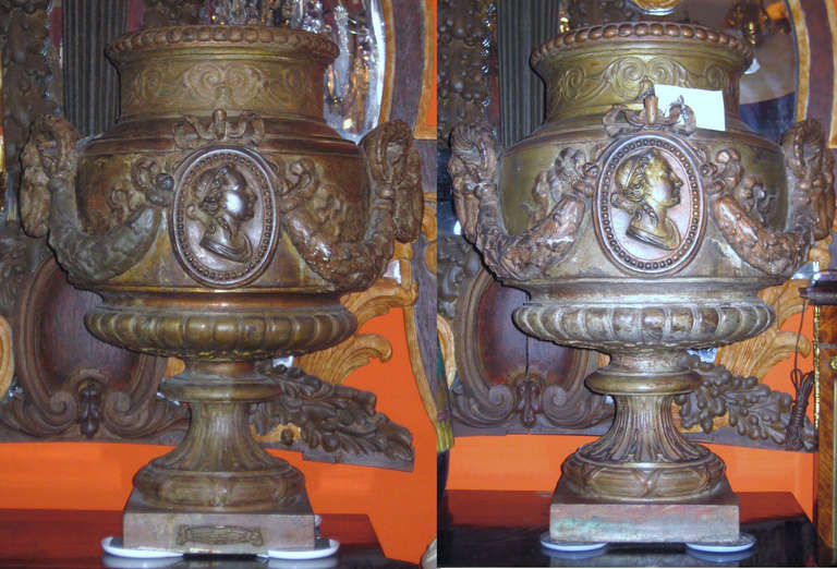Pair of large Val D' Osne cast iron urns, Paris, in the style of Louis XVI, campana form with gadrooned rim, neck with meandering foliage band, the front and back with a figural cartouche, applied rams-heads joining foliate swags raised on a short