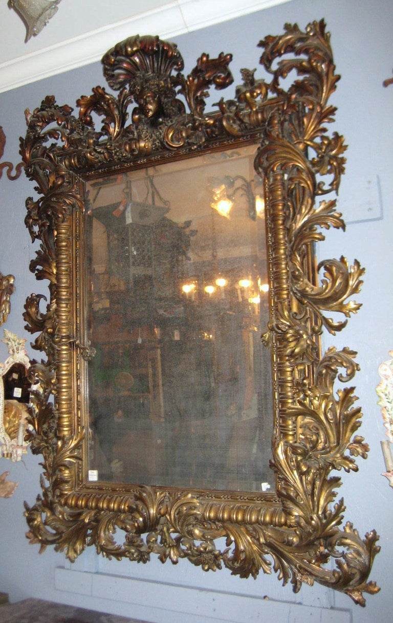 Large Baroque carved gilt-wood rectangular mirror, the crown centering a mask flanked by a scroll and foliate frame enclosing what appears to be the original beveled glass mirror. H: 74