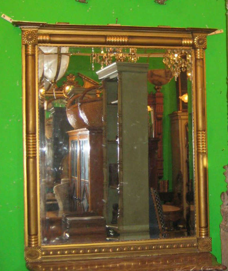 Pair of Regency style carved gilt-wood pier mirrors, having an overhanging molded cornice above a rectangular frame with patera corners and reeded columns enclosing the beveled glass mirror plate.