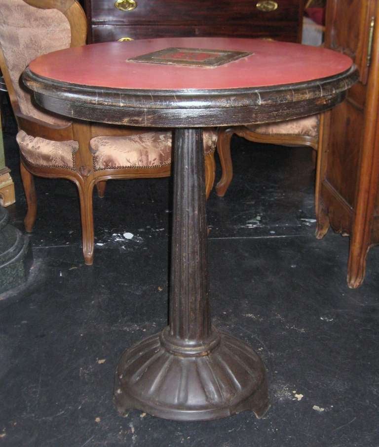 Authentic French Art Deco bistro (cafe) table, having a circular oak frame with laminate top and centering an inlaid tile, supported on an iron column and circular base. 

Note: A second table is available.