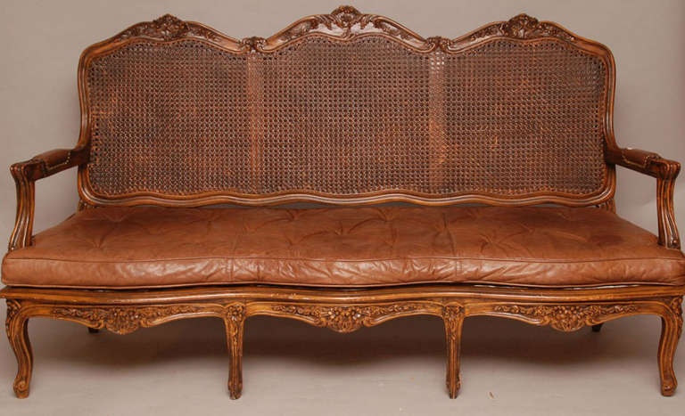 Provincial carved walnut three-seat double cane back settee with leather bench cushion.