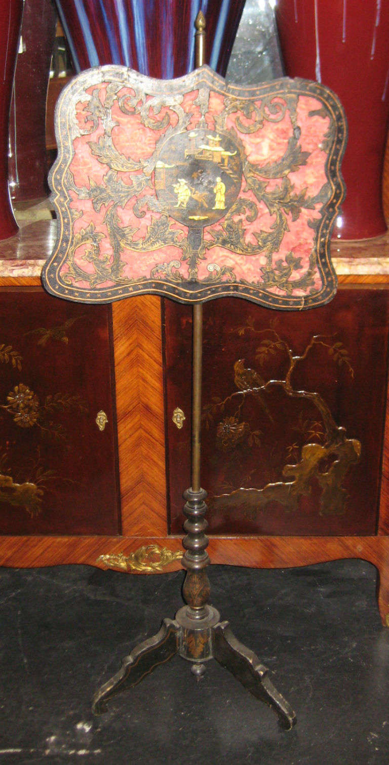 Chinoiserie and gilt decorated firescreen; the shaped rectangular adjustable screen centering a Chinoiserie decorated panel depicting a genre scene with figures, Phoenix bird and architectural structures in a landscape, the carved three-dimensional