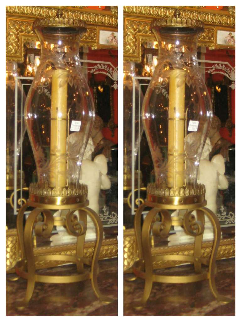 This is an extremely rare and fine pair of handblown etched glass hurricane lamps The baluster form glass shades etched with a floral design housing within a long candle, the iron base on four legs with ring support, the top with covers and flame