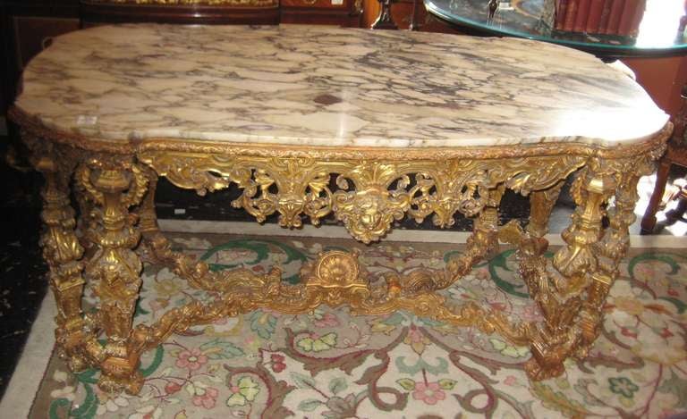 Louis XIV style highly carved gilt-wood marble-top center table (in the manner of similar François Linke tables) of shaped rectangular form, having a Breche de Violette marble top above a frieze of arabesques and flower heads centering a mask, the