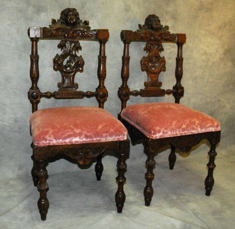 Pair of carved walnut side chairs, each with a putti mask and shell carved crest rail over a griffin carved splat flanked by acanthus leaf and fluted pilasters, carved seat rail on turned legs.