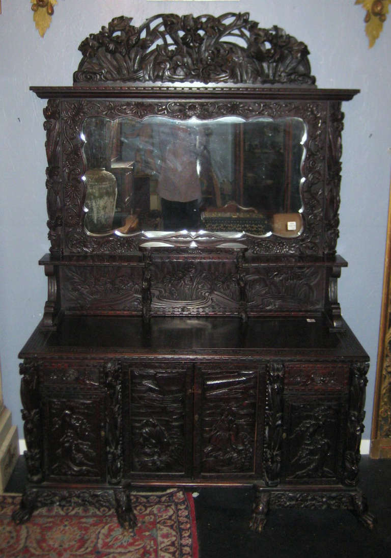19th century Japanese Meiji period ornately carved hardwood buffet, the upper part with a pierce carved cornice above a framed mirror with shelves; the lower part with a rectangular top above two figural carved cabinet doors flanked by two drawers