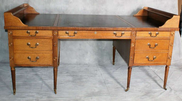 Martha Washington style mahogany five drawer desk with black tooled leather top and faux architectural drawers on the sides, raised on turned tapering legs terminating with brass wheels. 
