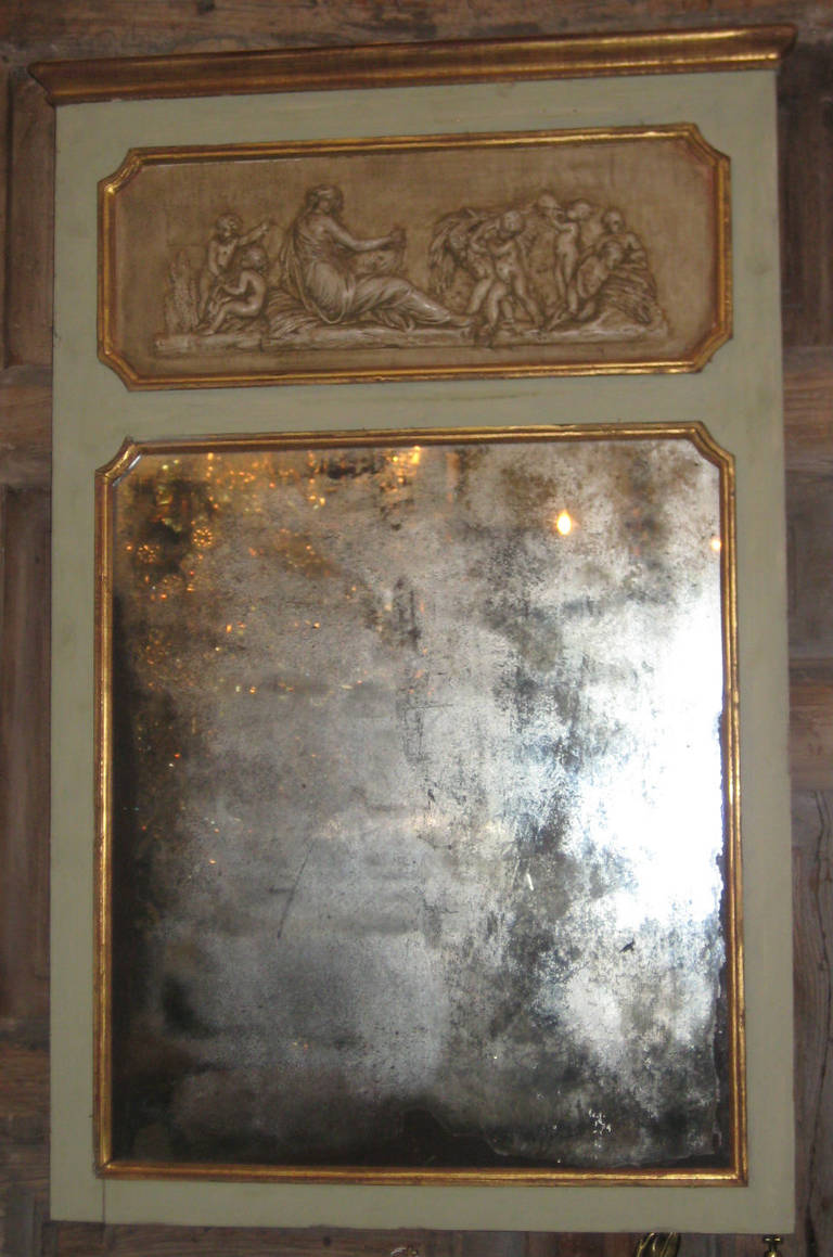 A petite trumeau mirror with pale green painted frame and cream painted carved bas-relief wood plaque depicting Harvest/Autumn over the origianal mirror plate with losses.