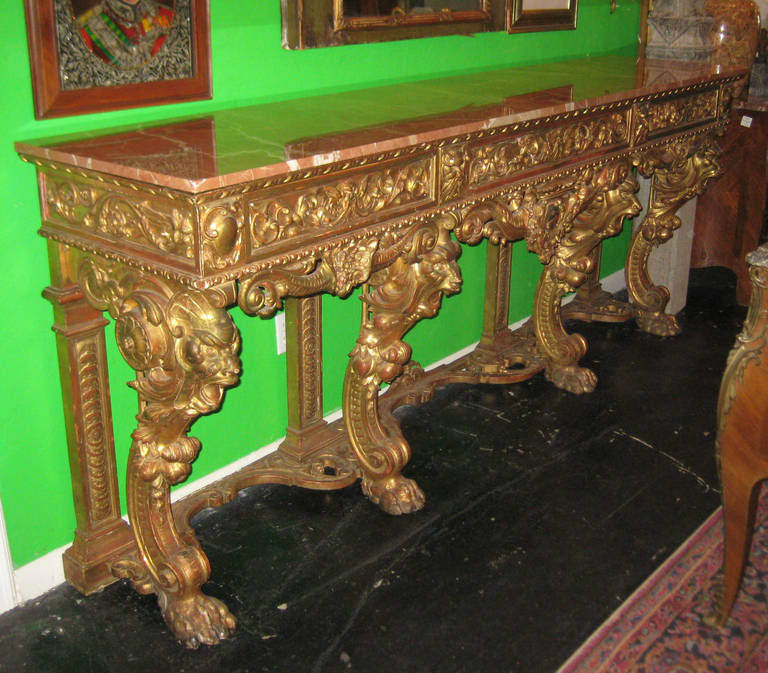 Large and impressive Italian carved gilt-wood marble-top console table; having a rectangular marble top over three carved frieze drawers and centering a crowned polychrome crest on four Griffin-form legs joining a stretcher support.