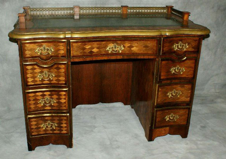 19th c. Louis XV/Louis XVI Kingwood and stainwood parquetry inlaid kneehole desk, having a shaped rectangular top with molded bronze banded edge, inset green leather writing surface, and bronze gallery rail, over a center frieze drawer flanked by