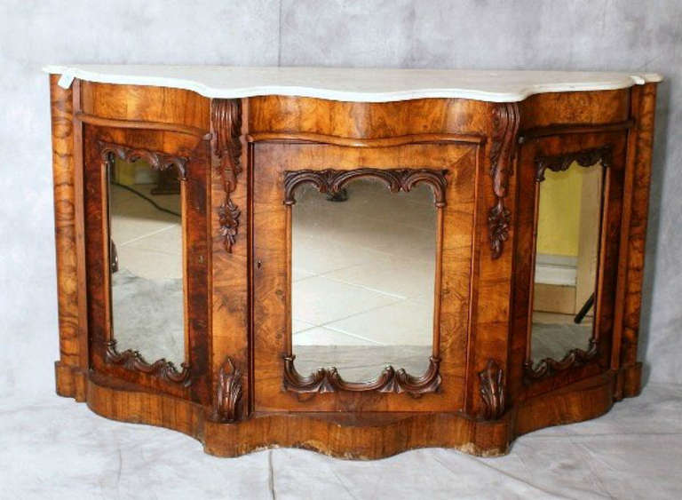 English Victorian caved walnut and marble-top credenza, having a shaped white marble top over a conforming cabinet with three mirror fronted doors on a plinth base.