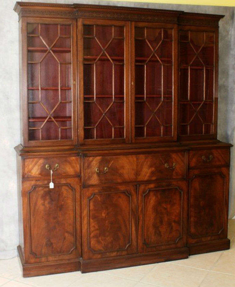 Chippendale mahogany two-part breakfront secretary, the upper section having a dentil molded cornice above a carved frieze over four mullioned glass doors, the lower section centering a desk drawer opening to an interior with valanced cubby holes