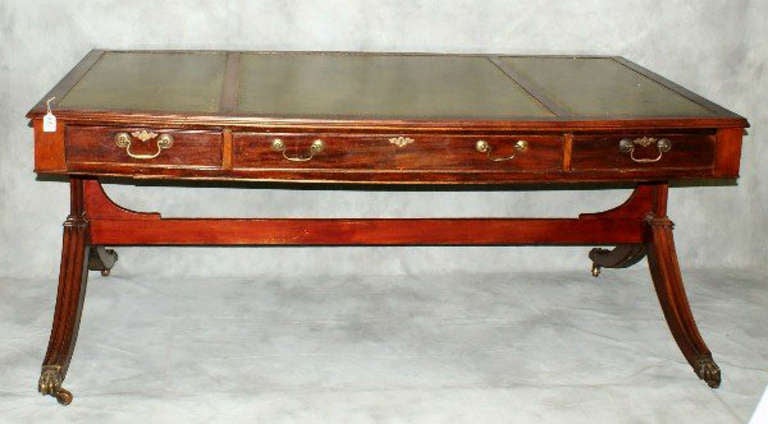 Regency mahogany library table having a rectangular tooled leather top above a long center frieze drawer flanked by short drawers with brass handles raised on a stretcher base with down swept legs terminating with brass paw and casters, locks signed