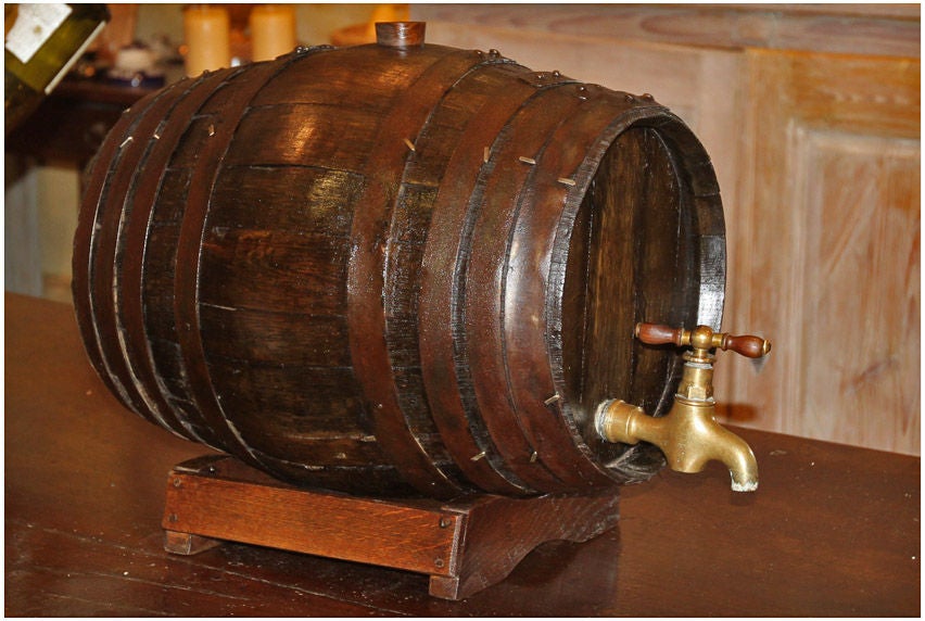 19TH CENTURY WOODEN TONNEAU (WINE CASK) WITH BRONZE SPIGOT AND WOODEN BASE. USED FOR THE PRESENTATION OF THE WINE.  HAS INTERESTING METAL BRADS TO HOLD METALBINDING BANDS IN PLACE.  FROM THE BURGUNDY AREA, CIRCA 1890.<br />
H (WITH STAND) 14½