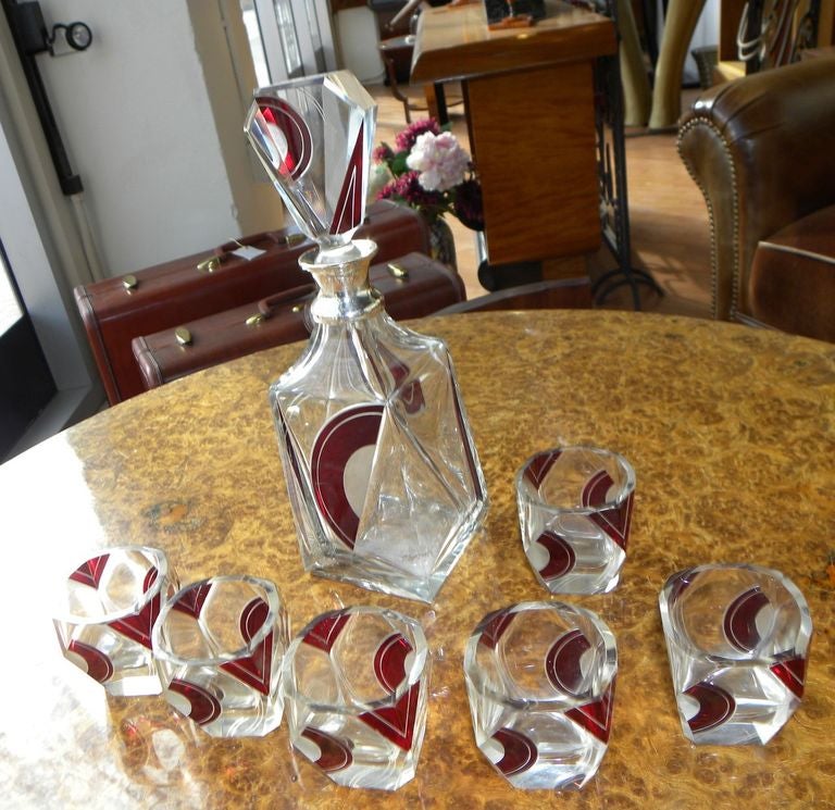 This 1930s Art Deco Czech Decanter Set boasts a very rare unusual shape with a wonderful design that artistically plays with positive and negative space. The glasses bear a ruby red enameled design that is both modernist and geometric. Perhaps a