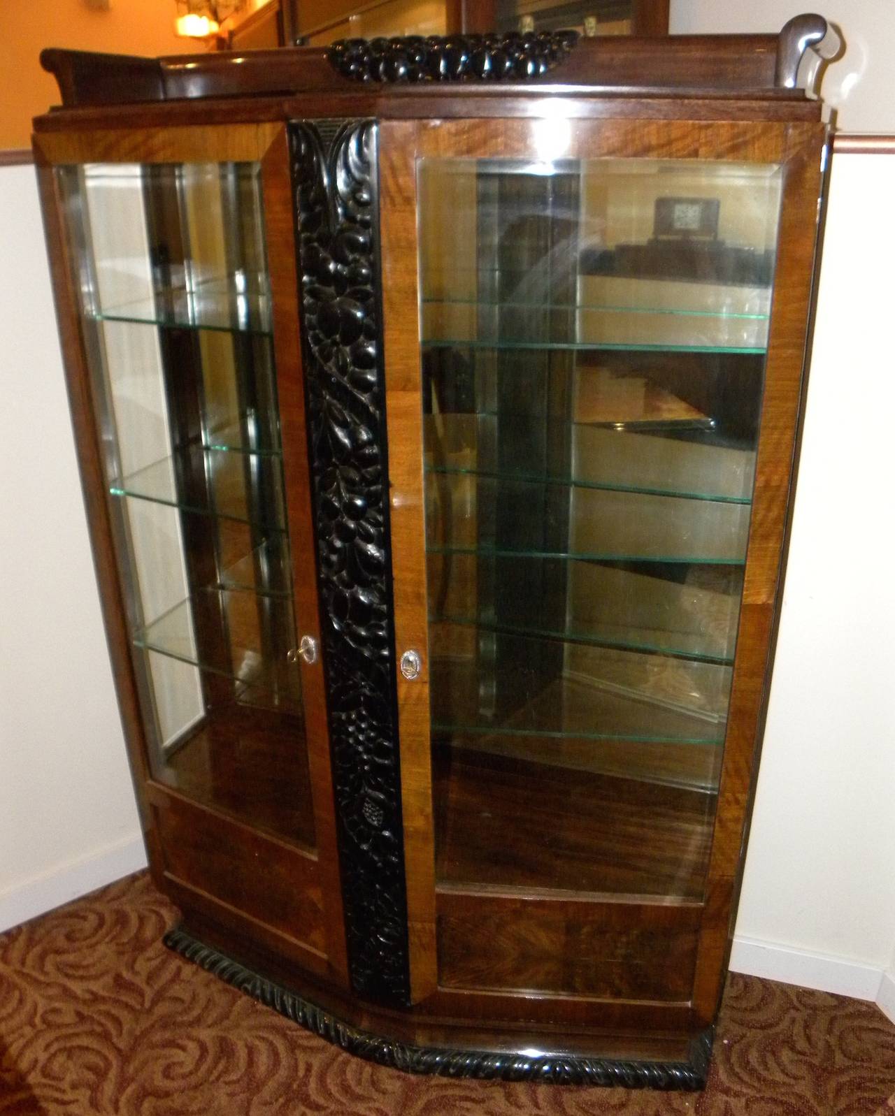 This display cabinet in walnut with glass front boasts a rich, dark, carved wood embellishment as it’s frontispiece. What better way to show off your collected treasures than this good sized vitrine with its polished edge glass shelves and beveled