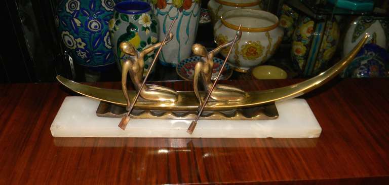 Unusual bronze statue depicting two woman with oars rowing a boat on the water. In the style of Hagenauer but not signed. The bronze is sitting on a marble base and the area just beneath the boat has a stylized water relief. In excellent original