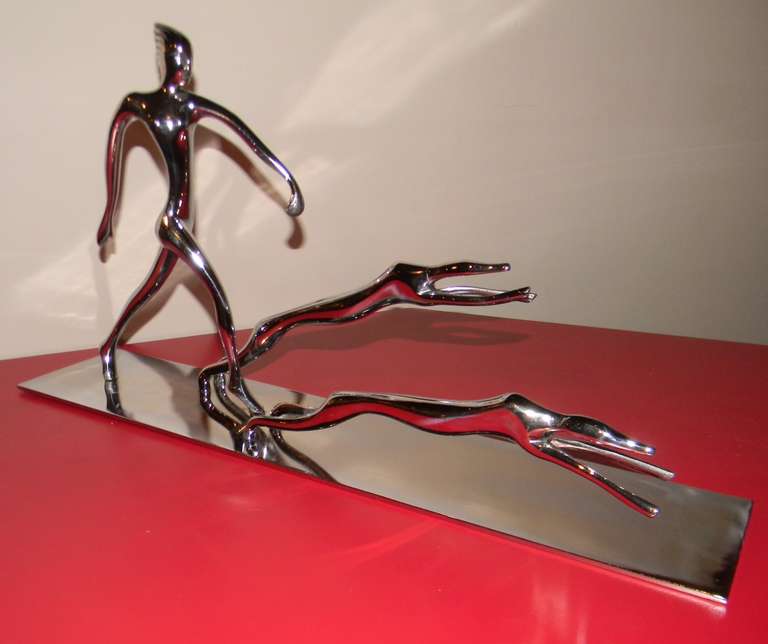Stylized statue of a woman with leaping dogs. Could be greyhounds both the dogs and woman have a very unique stylized art deco rendering. The piece is chrome on simple but strong metal plate. Very unique and original work of art deco statue.