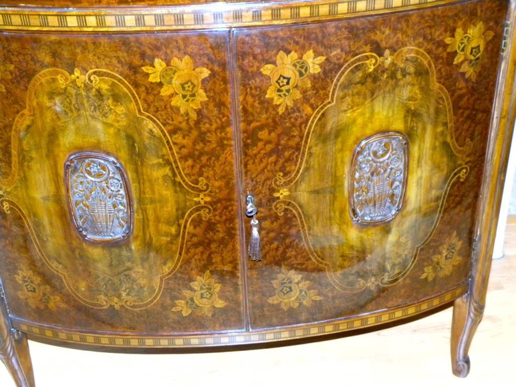 This a wonderful Classic French early 1920s Art Deco demilune style storage cabinet. Please take special note of the wonderful floral marquetry in four panels on the front and side doors. The legs are very reminiscent of the designs of Paul Follet,