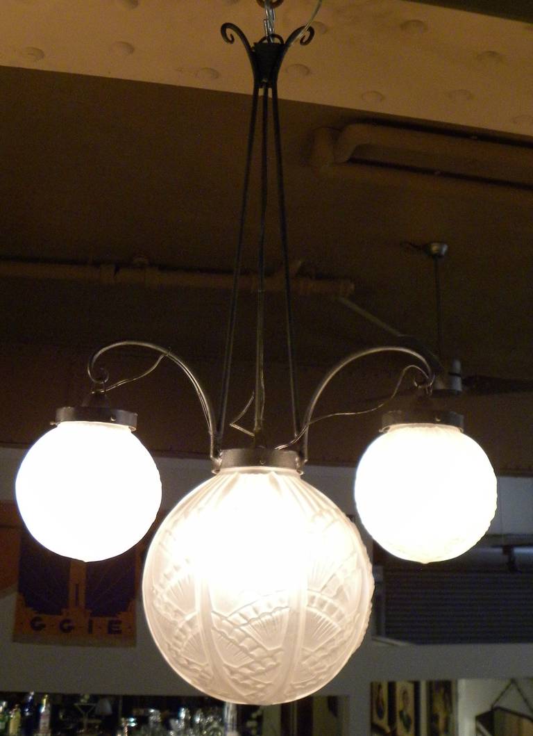 A voluptuous French Art Deco pressed glass chandelier suspended in ironwork with four globes in high style patterns.

It was during this period, the early 1920s that great ironwork was combined with such fabulous frosted and pressed glass lighting