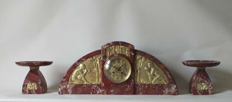 Huge original Art Deco French pendulum clock with matching garnitures or side pieces, circa 1925. This is an especially high quality example with artist signed (G. Mourac) gilt bronze relief panels and marble is a stunning rouge color. The panels