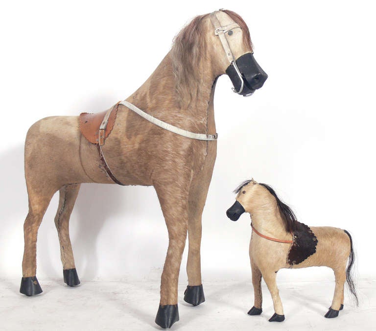 Two Antique Horses, age unknown. We originally thought they were 19th century, but more likely are early 20th century examples. Outstanding decorative forms. Constructed of actual horsehide, wood, and leather. The larger horse measures 35