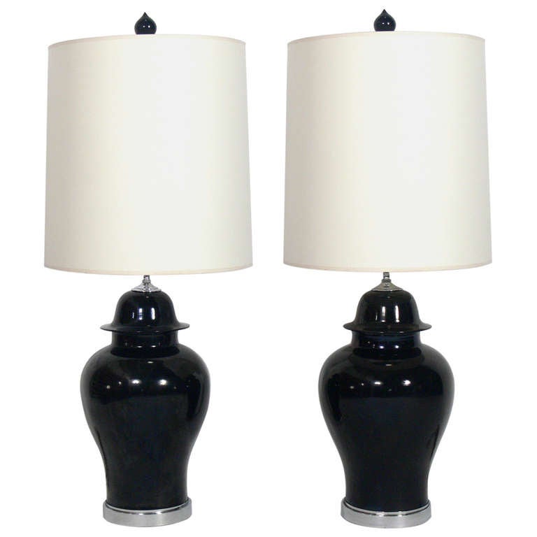 Asian Urn Form Ceramic Lamps, American, circa 1970's. One pair constructed of black ceramic urns with chrome plated metal fittings. They retain their original ceramic finials. The black urn lamps measure 42