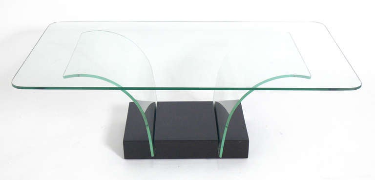 Table basse en verre sculptural, conçue pour la Modernage Company de New York, vers les années 1940. La base en bois a été refinie dans une laque de couleur marron très profonde. Conserve les supports en verre et le plateau de table d'origine.