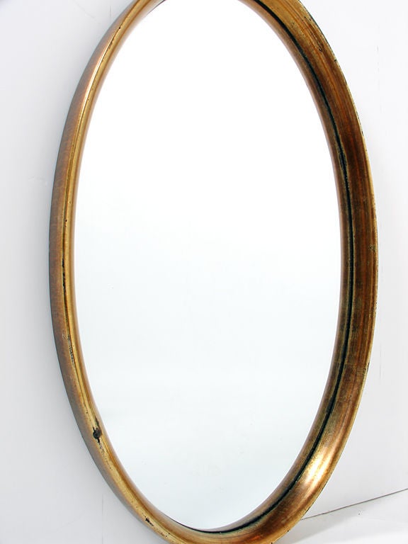 Modernist Oval Gold Leaf Mirror, American, circa 1960's. It exhibits wonderful patina and wear to the gold leafing, beautifully exposing a bit of the black bole or underlayer. This mirror has a sculptural form and would fit seamlessly into a wide