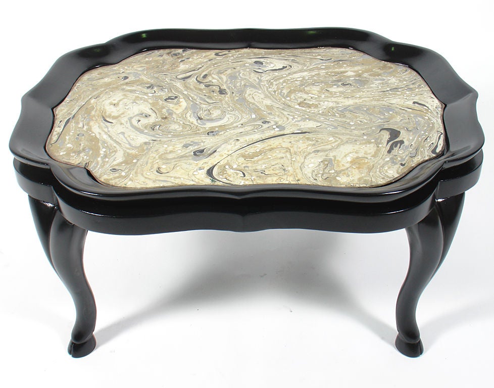 Élégante table basse, probablement américaine, vers les années 1940, avec des pieds zoomorphes galbés et conservant son incroyable plateau en verre marbré peint à la main, exécuté dans des tons or, argent et noir.